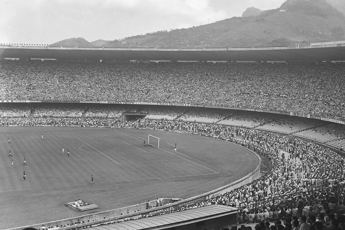 Uma fotografia a preto e branco de um jogo no Maracanã antes do Campeonato do Mundo de 1950, com as bancadas cheias de multidão e uma montanha ao fundo do estádio
