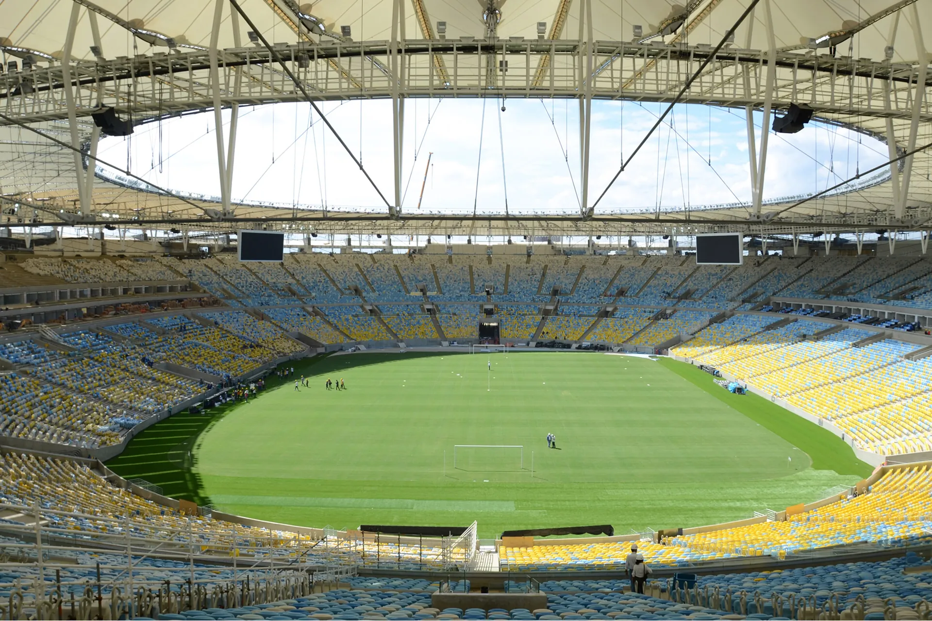 Interiér stadionu Maracanã v Riu de Janeiru s tribunami žlutých, modrých a bílých sedadel kolem zeleného hřiště pod prstencovou střechou